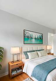 A bedroom with a bed, nightstand, and a painting on the wall.