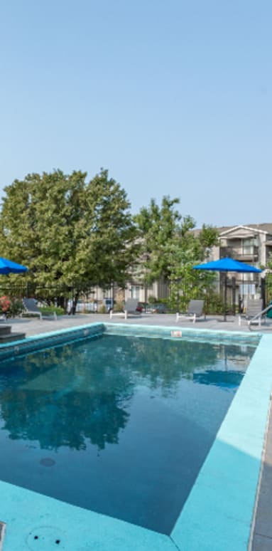 A swimming pool surrounded by a stone wall and blue umbrellas.