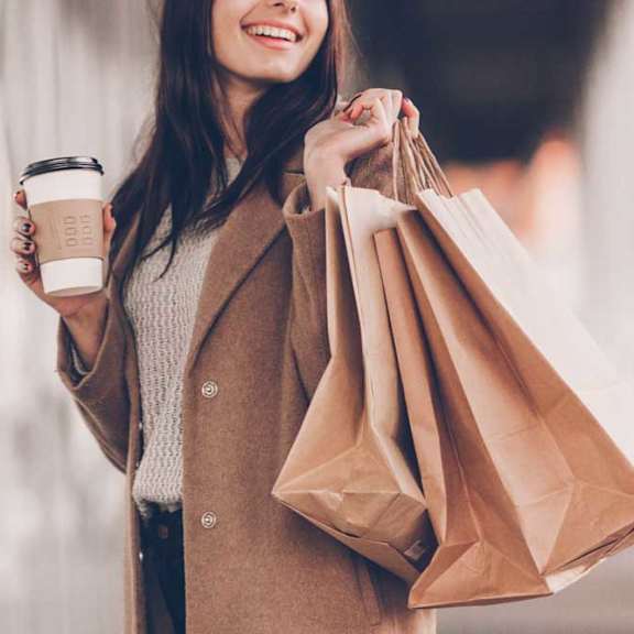 A woman is holding a cup of coffee and shopping bags.