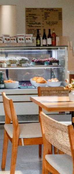 A restaurant with wooden tables and chairs and a display case filled with pastries and bottles.