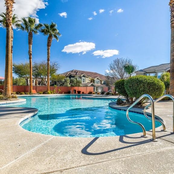 our resort style swimming pool with palm trees and buildings in the background