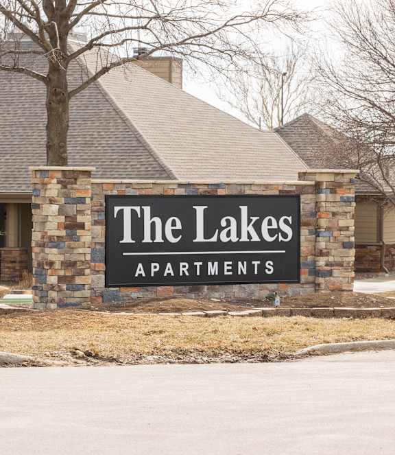 The Lakes apartment complex entrance sign with a stone-brick backing and the clubhouse visible in the background.