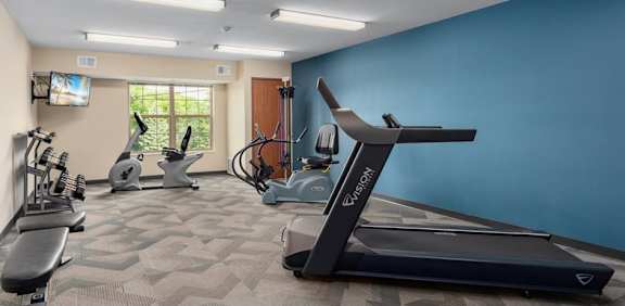 A spacious gym with a variety of exercise equipment including treadmills, stationary bikes, and rowing machines.