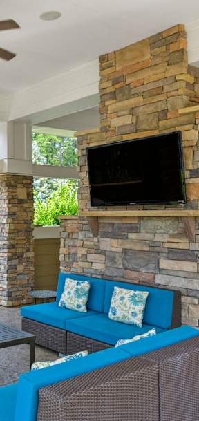 A patio with a blue couch and a stone fireplace.