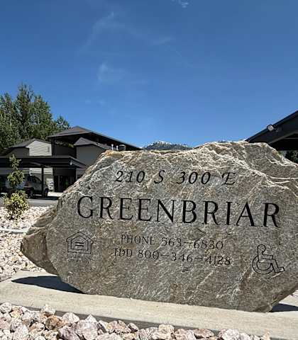 A stone sign with the name GREENBRIAR and contact information is in front of a building.