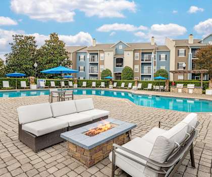 A poolside area with a couch, chairs, and a fire pit.