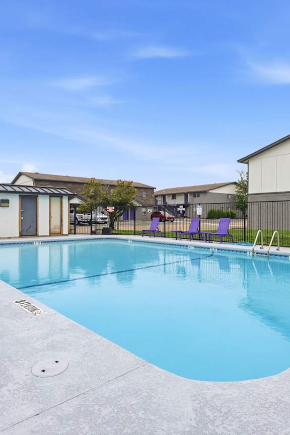 A large outdoor swimming pool with purple lounge chairs.