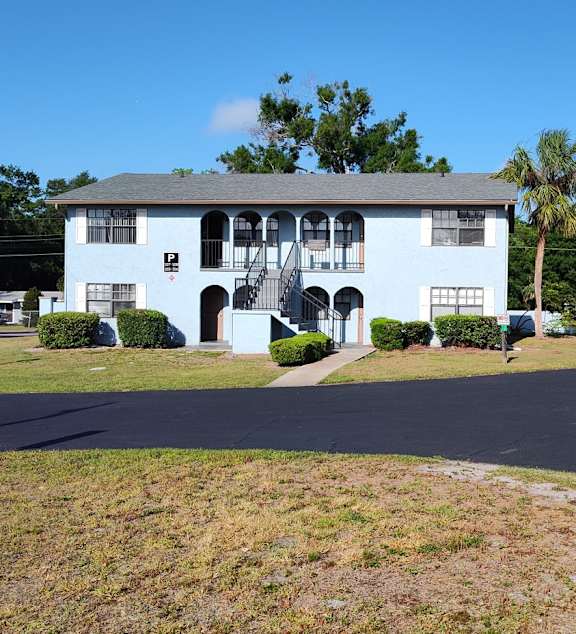 A white building with a blue roof and a large lawn in front of it.