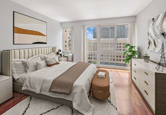 A bedroom with a large bed, a nightstand, and a window overlooking a cityscape.