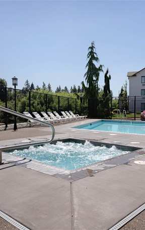 An outdoor hot tub next to a swimming pool and lounge chairs at Riverplace Apartment Homes, Independence, 97351