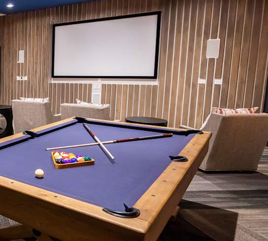 A pool table is in the middle of a room with a couch, a coffee table, and a TV.