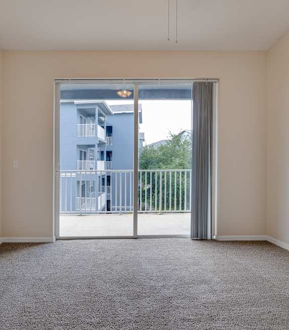 A room with a carpeted floor and a sliding glass door leading to a balcony.