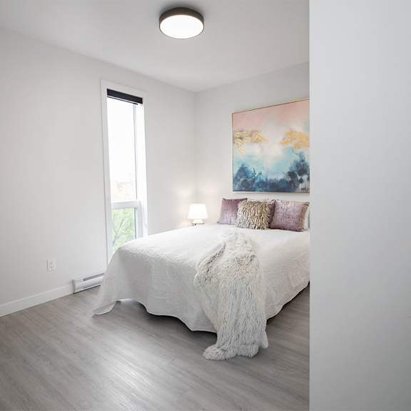 A bedroom with a large bed, a painting on the wall, and a wooden floor.