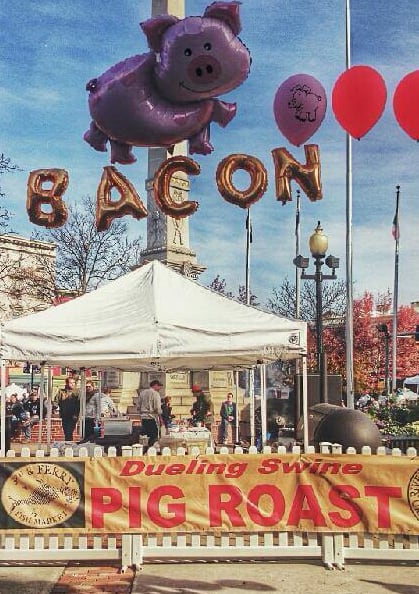 a group of people standing in front of a pig roast sign