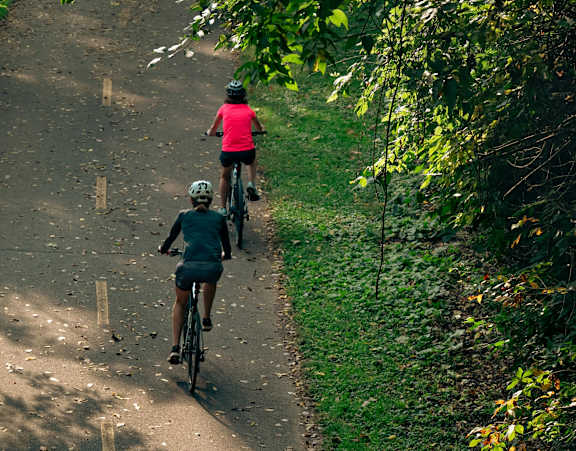 Two people riding bikes on a path surrounded by trees.