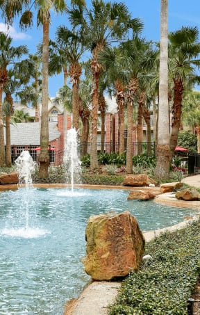 a fountain in the middle of a pool with palm trees