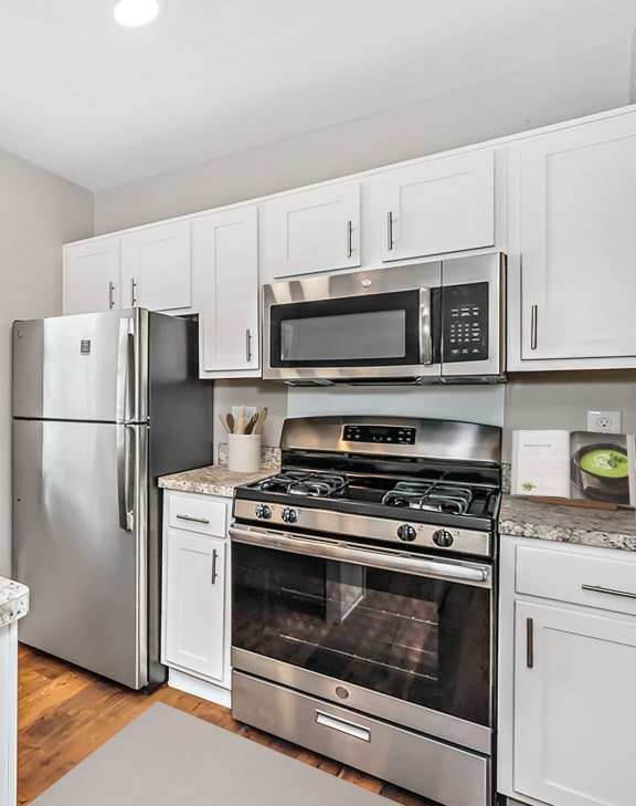 a kitchen with white cabinetry and a granite counter top with a bowl of fruit on it at Staples Mill Townhomes, Richmond, VA