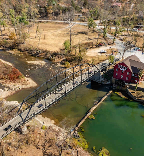 A red building is situated next to a metal bridge over a green body of water.