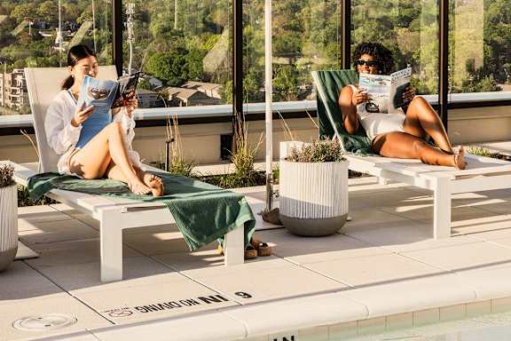 Two people are sitting on lounge chairs by a pool, reading books1 at Scout Living, powered by Placemakr, Atlanta