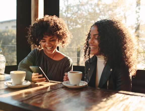 two women sitting at a cafe table looking at a cell phone