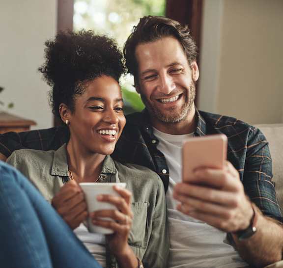 a man and woman sitting on a couch looking at a cell phone