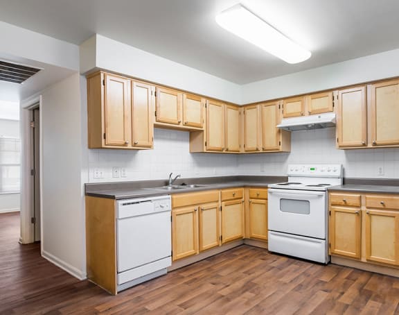 an empty kitchen with white cabinets and hardwood like flooring at Horace Mann Apartments and townhomes in Gary, IN