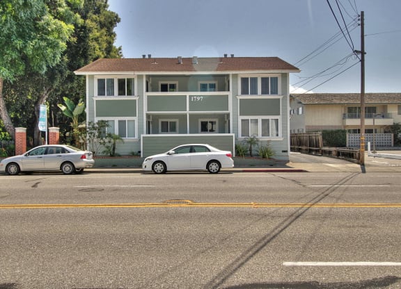 Two cars are parked in front of a white building with a red roof.