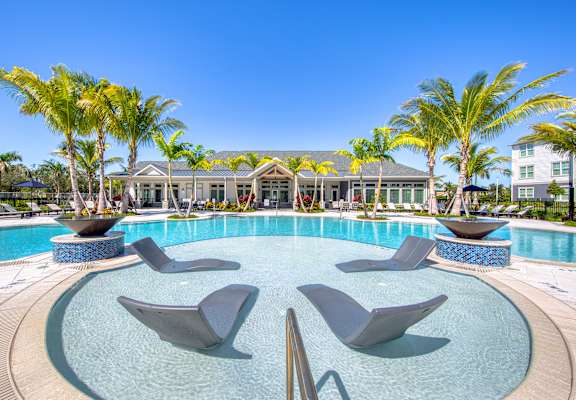 a swimming pool with chairs and palm trees in front of a hotel