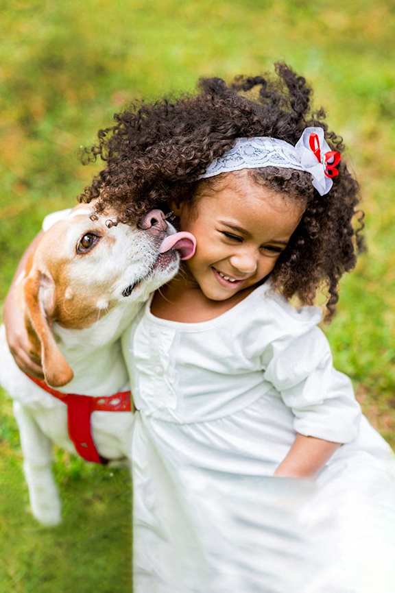 A little girl in a white dress is hugging a dog.