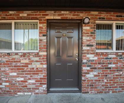 A brown door with the number 13 on it is on a brick wall.