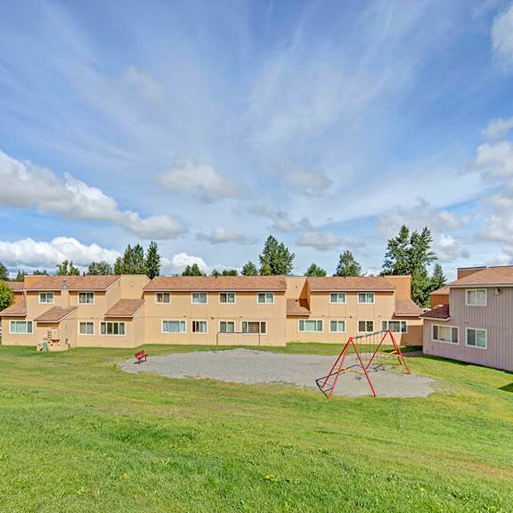 The exterior of the orange apartment homes with a playground and green grass lawn at the Glen Apartment Homes. 