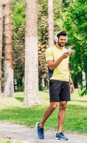 A man in a yellow shirt and blue shoes is walking on a path in a park.