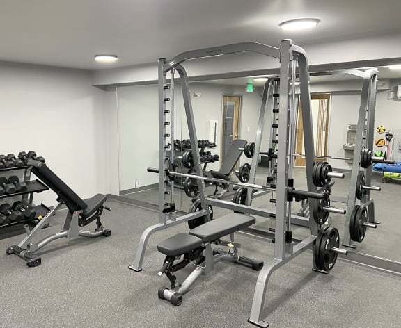 a fitness center with many free weights, two benches, a bench press and a large mirror on the wall at University Glen, University Place, Washington