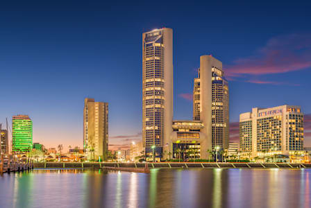 A cityscape at dusk with buildings reflecting on the water.