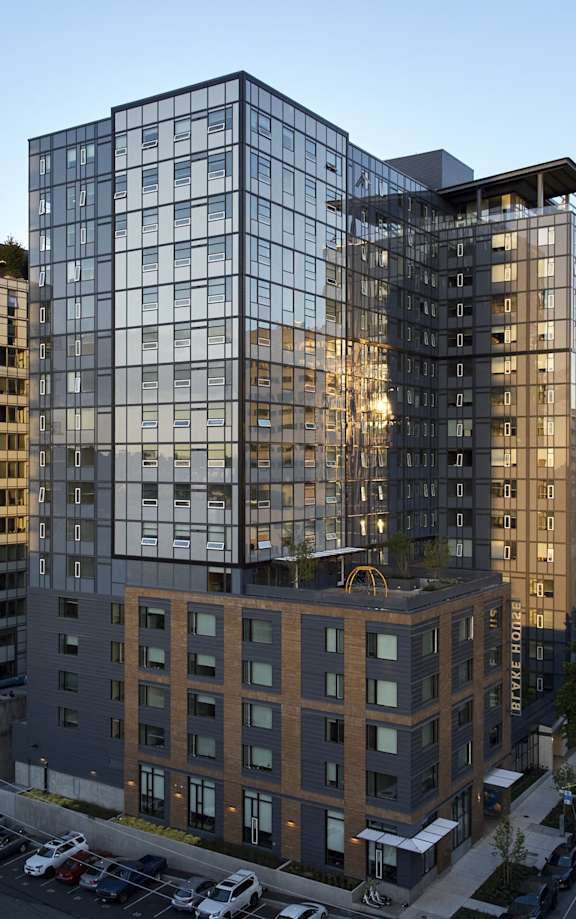 A modern glass building is reflected in the glass facade of the building next to it.
