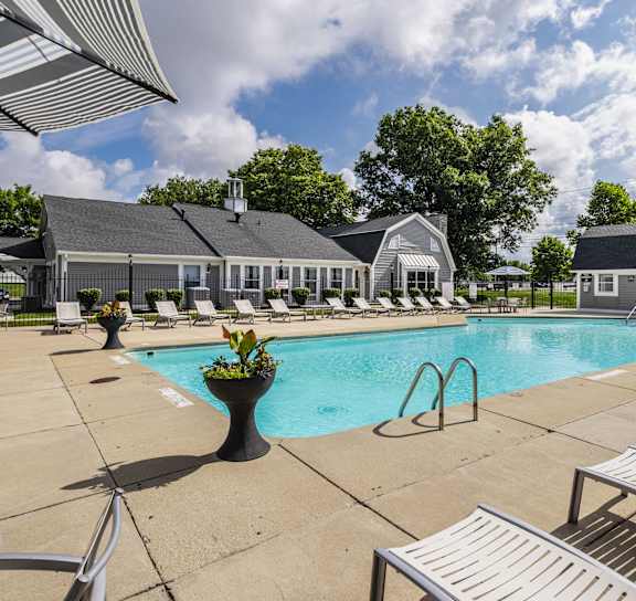 a pool with lounge chairs and a house in the background at Bay Pointe Apartments in IN 47909