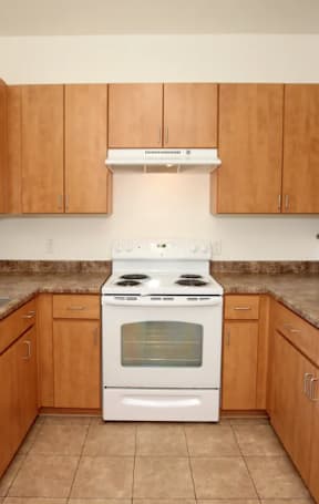 A kitchen with a white stove top oven and wooden cabinets.