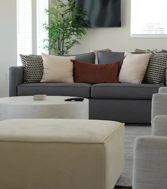 A grey couch with pillows and a white ottoman in a living room.