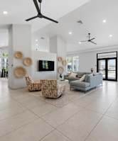 A spacious living room with a grey sofa, a white armchair, and a TV on the wall.