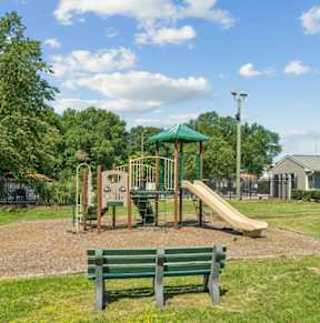 A playground with a green slide and two benches.