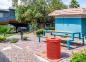 Thumbnail 17 of 23 - Fifteen 50 apartments Las Vegas courtyard with modern blue picnic table, market lights, red trash can, and barbecue next to small blue structure.