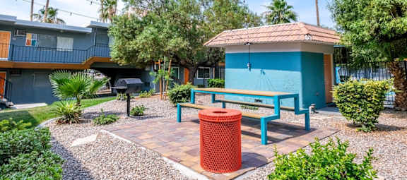 Fifteen 50 apartments Las Vegas courtyard with modern blue picnic table, market lights, red trash can, and barbecue next to small blue structure.