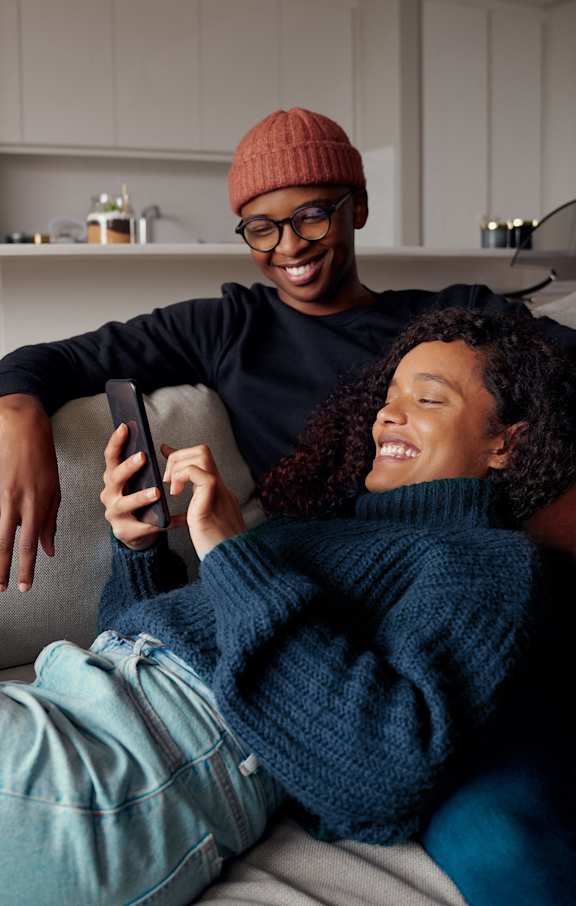 A man and a woman are sitting on a couch, with the man holding a remote control.