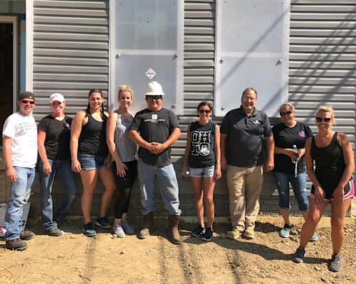 A group of people are standing in front of a grey building.