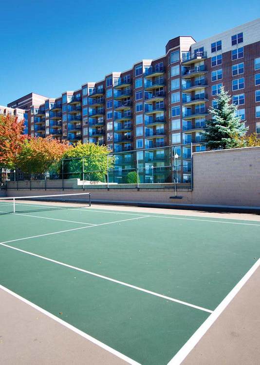 A tennis court is surrounded by apartment buildings.
