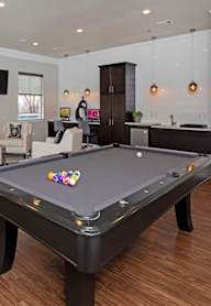 A pool table is in the middle of a room with a bar and a couch.