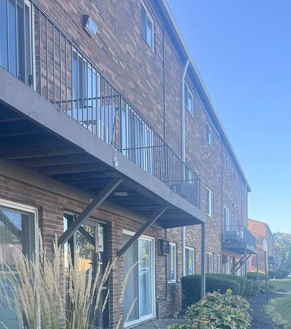 A building with a balcony and a small garden in front. at Garfield Villa Apartments, Garfield Heights, Ohio