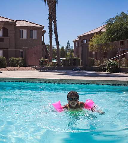 A boy swims in a pool with pink floaties.