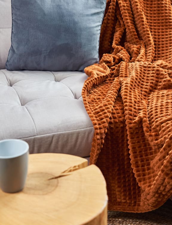 a couch with a blanket on it and a coffee cup on a table