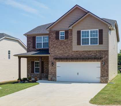 A two-story house with a garage is surrounded by a grassy area and a sidewalk.